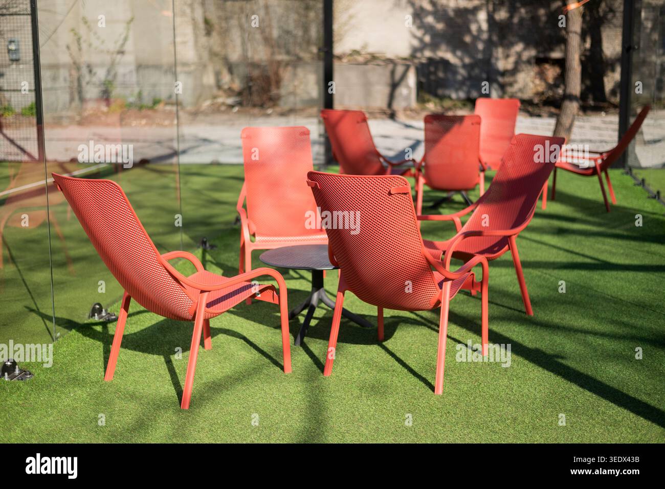 Modern red lounge chairs arranged around a table on artificial green grass in a bright outdoor patio area. Stock Photo