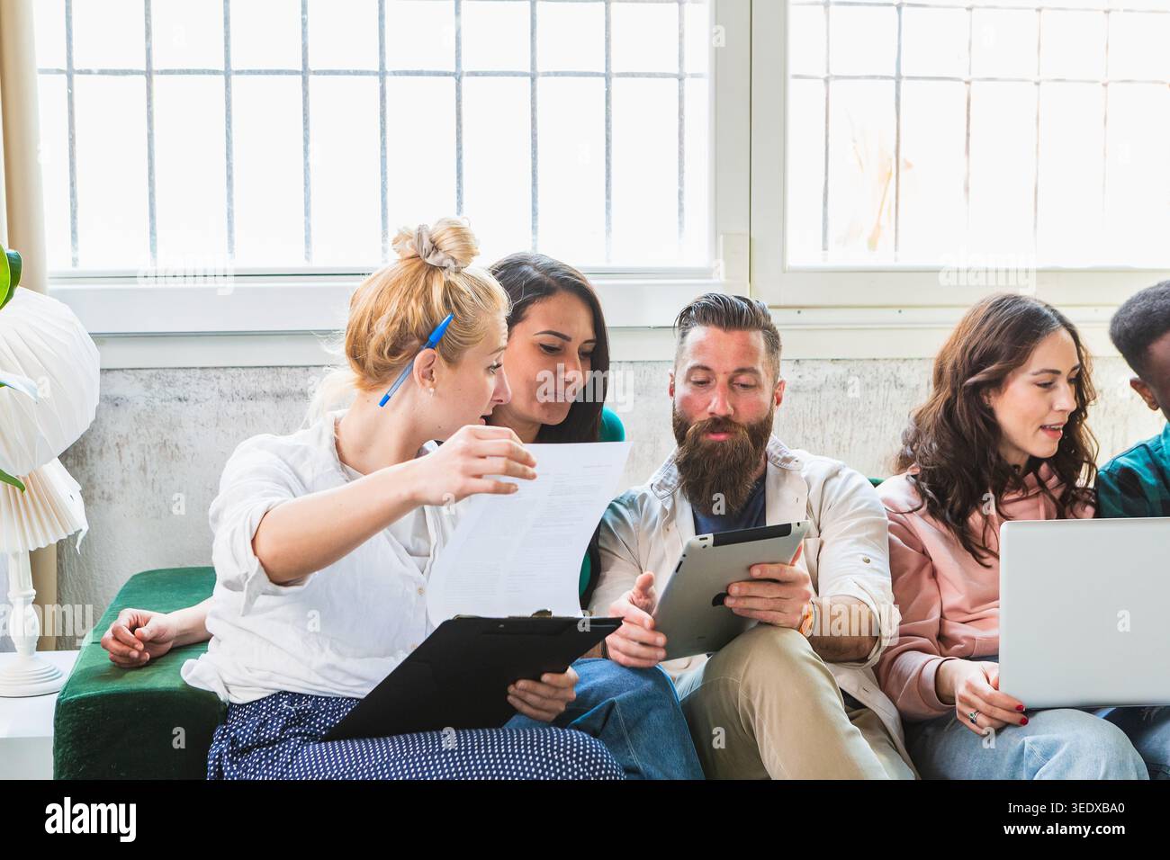 Diverse group of students working together on a project, analyzing documents and using digital devices Stock Photo