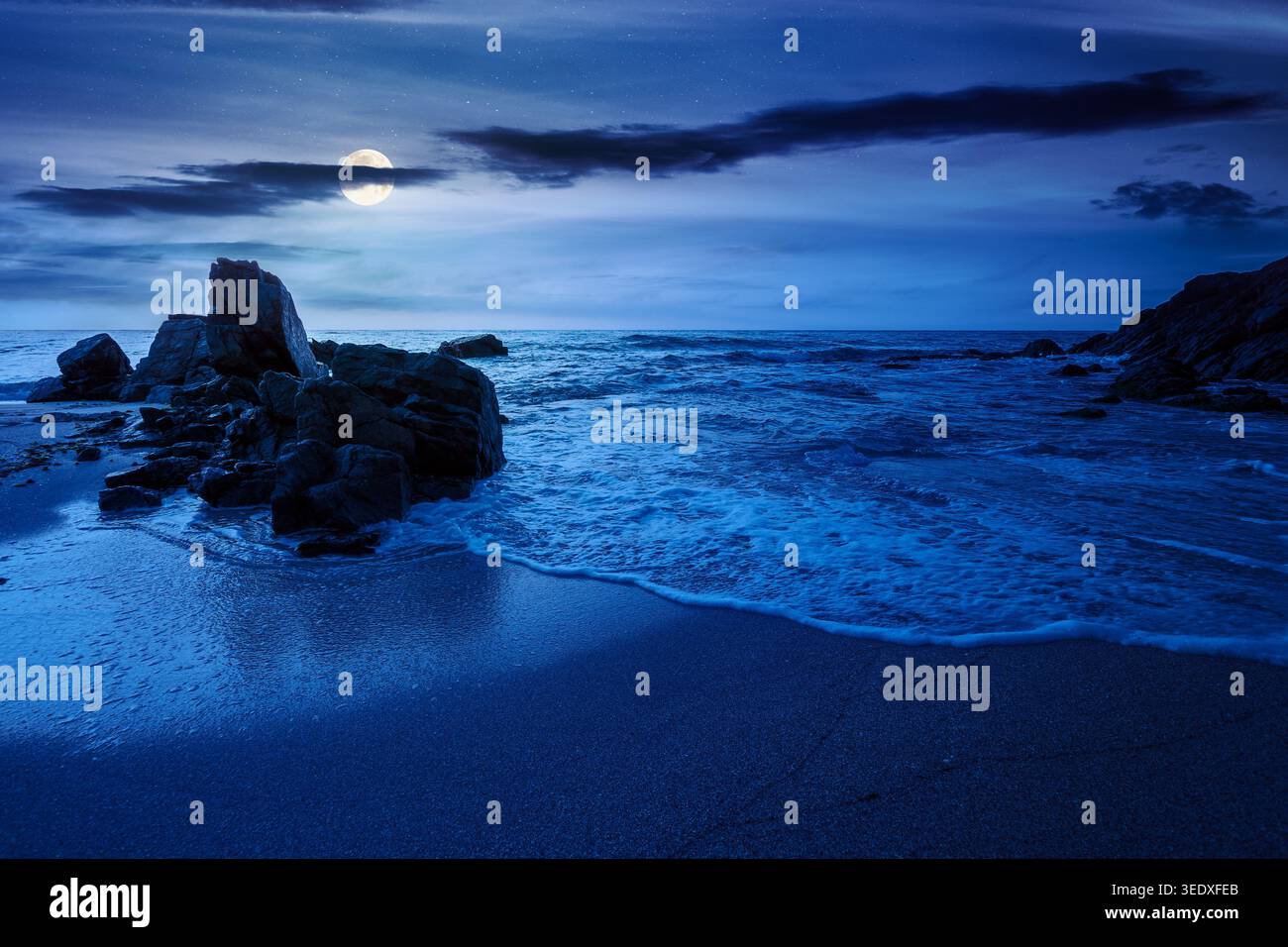 huge stones on the sandy beach at night. mysterious holiday season background at the sea. full moon over clouds on the dark sky above horizon. view of Stock Photo