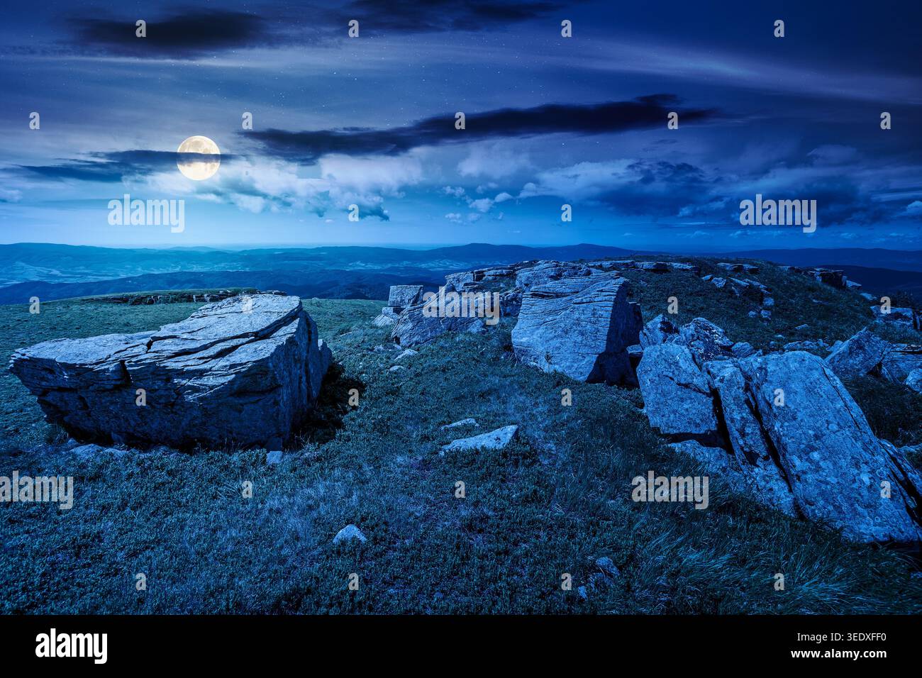 mountainous landscape during summertime at night. full moon over boulders and rock formations surrounded grassy hills. picture of an untouched highlan Stock Photo