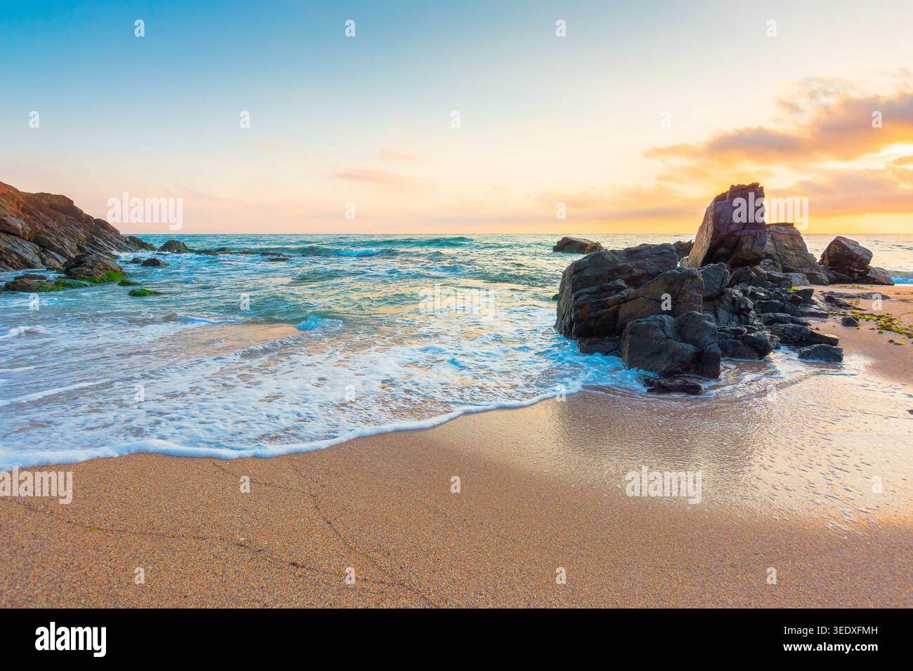 huge stones on the sandy beach at sunrise. wonderful holiday season background at the sea. clouds on the blue sky above horizon. view of waves washing Stock Photo
