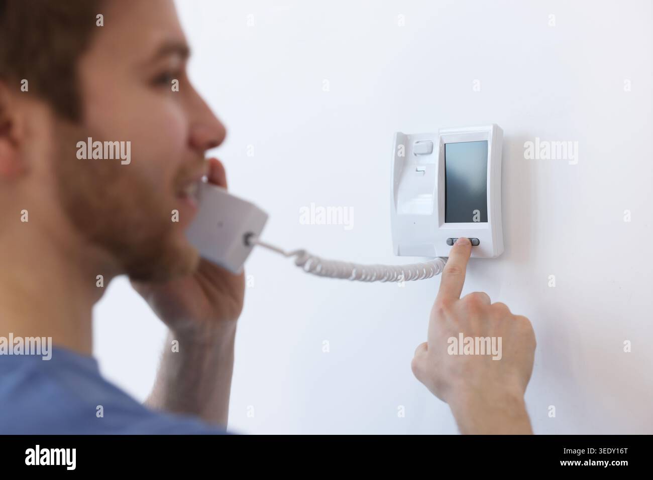 Man with handset pressing button on intercom panel indoors, closeup Stock Photo