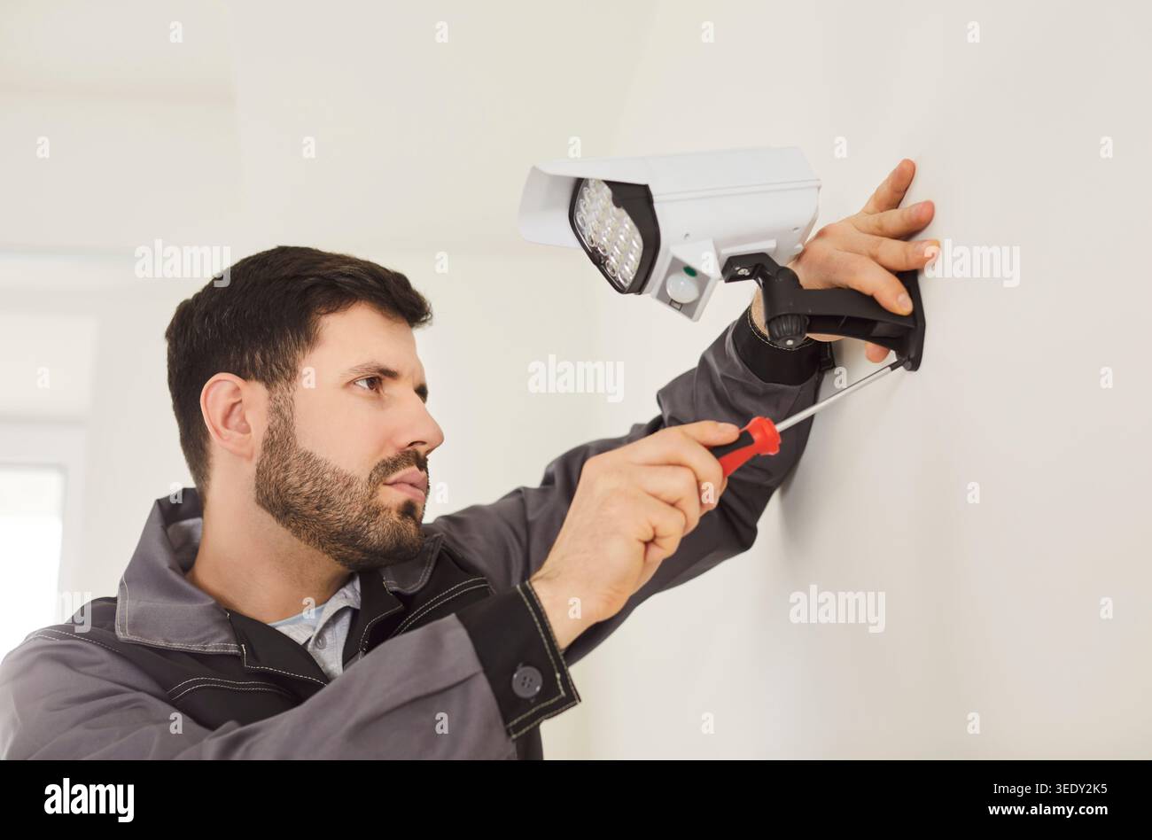 CCTV indoor wall setting, installing security camera, man holding screwdriver, fastening mount wall Stock Photo