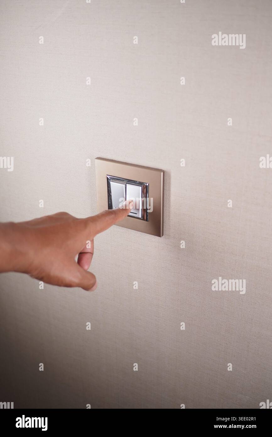 Hand pressing a light switch on a wall in a room Stock Photo