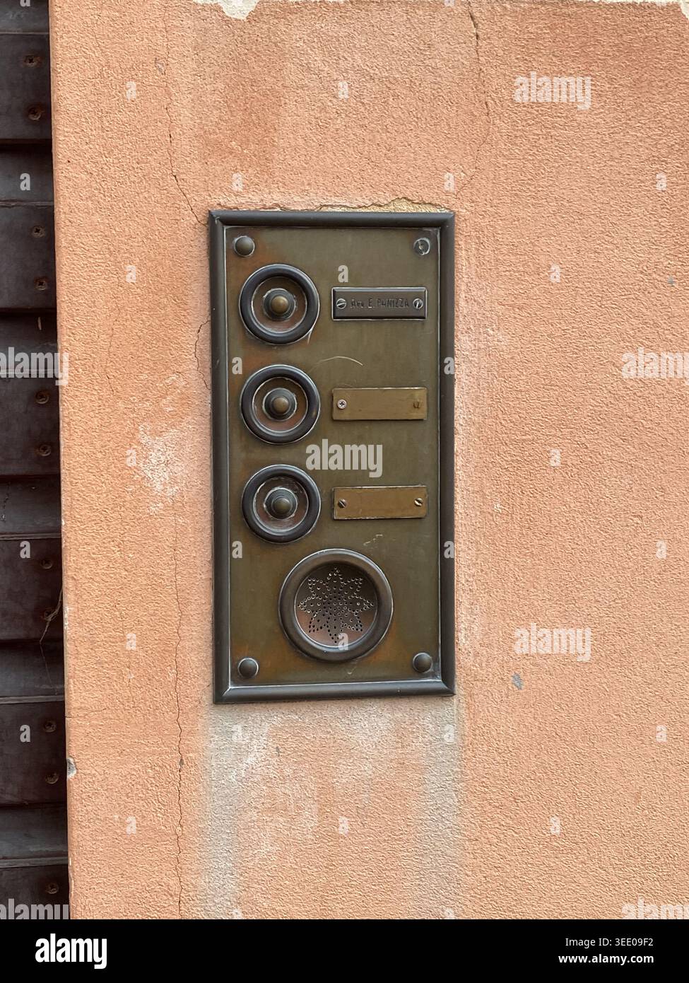 Ornate vintage brass doorbell and intercom panel mounted on a weathered peach stucco wall, showing aged patina, multiple buttons and speaker at a home Stock Photo