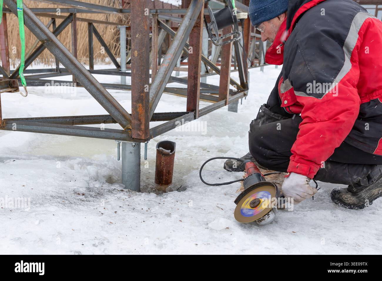 Worker using angle grinder on metal construction during winter outdoor repair work Stock Photo
