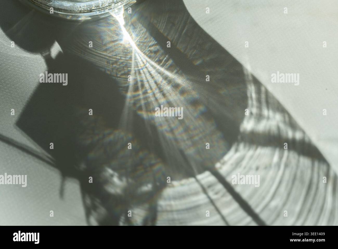 Abstract sunlight reflection created by glass object casting textured shadow and rainbow light patterns on white surface. Minimal artistic composition Stock Photo