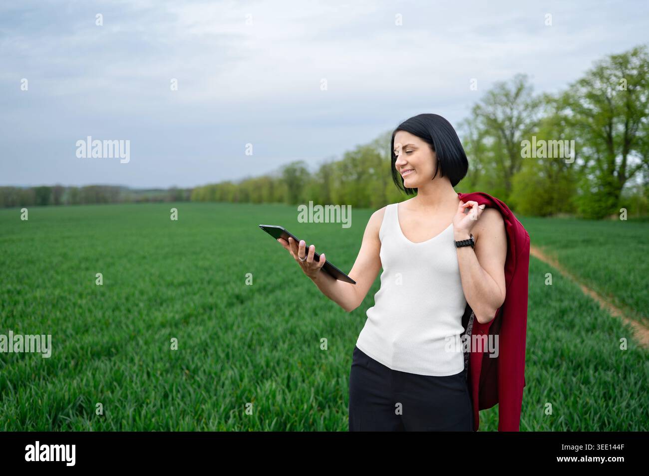 Woman using tablet while standing in green field outdoors Stock Photo