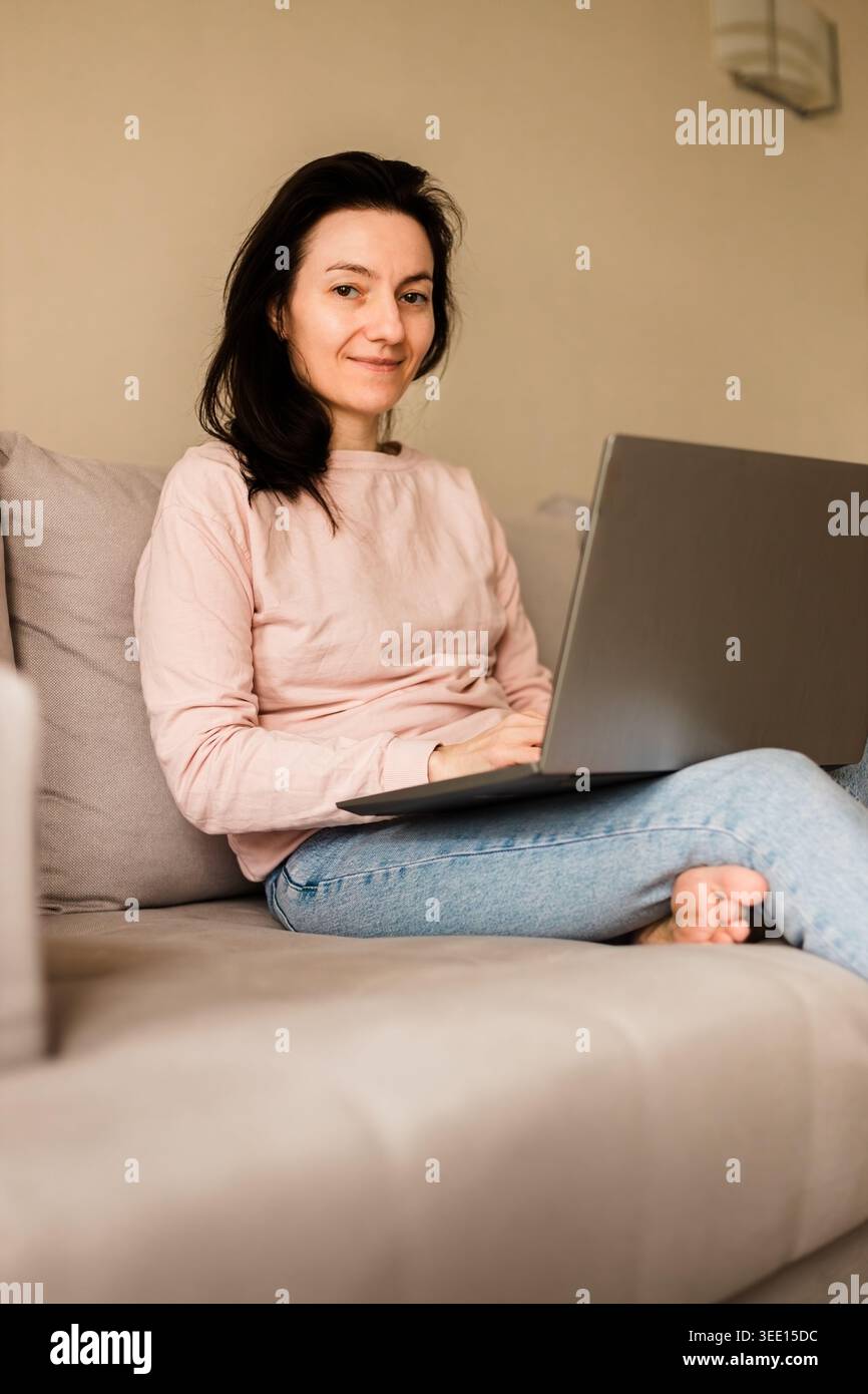 Cheerful female freelancer using computer at home on comfortable couch Stock Photo