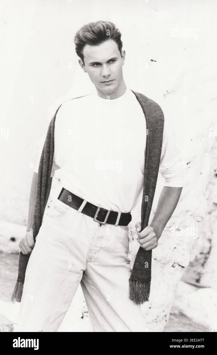Black and white full-length portrait of a young male model standing confidently with a dark knitted scarf draped over his shoulders Stock Photo
