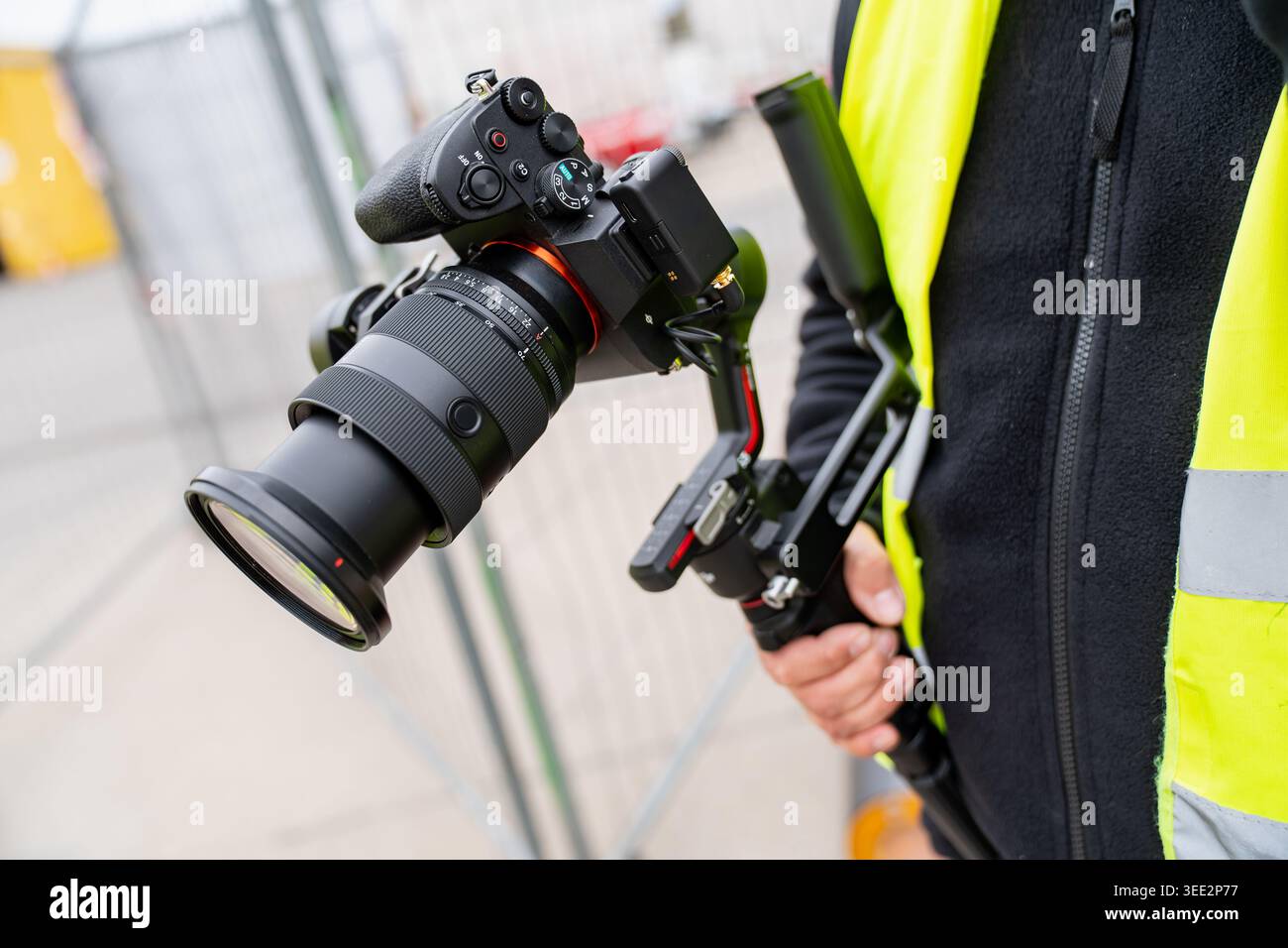Videographer using a digital camera with a large lens and electronic steadycam system for high quality content production at a construction facility w Stock Photo