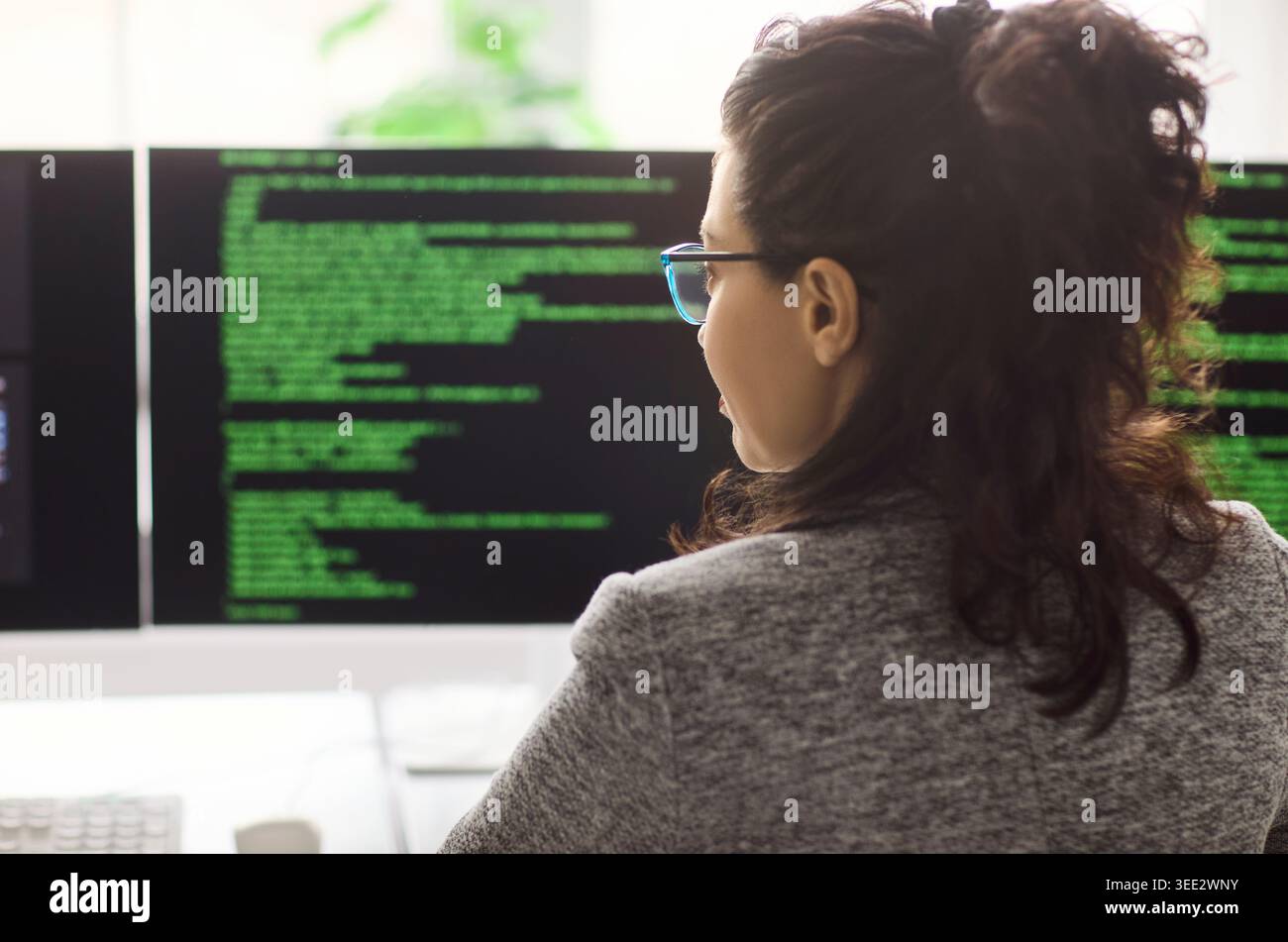 Female software developer coding at computer with dual monitors in modern office Stock Photo
