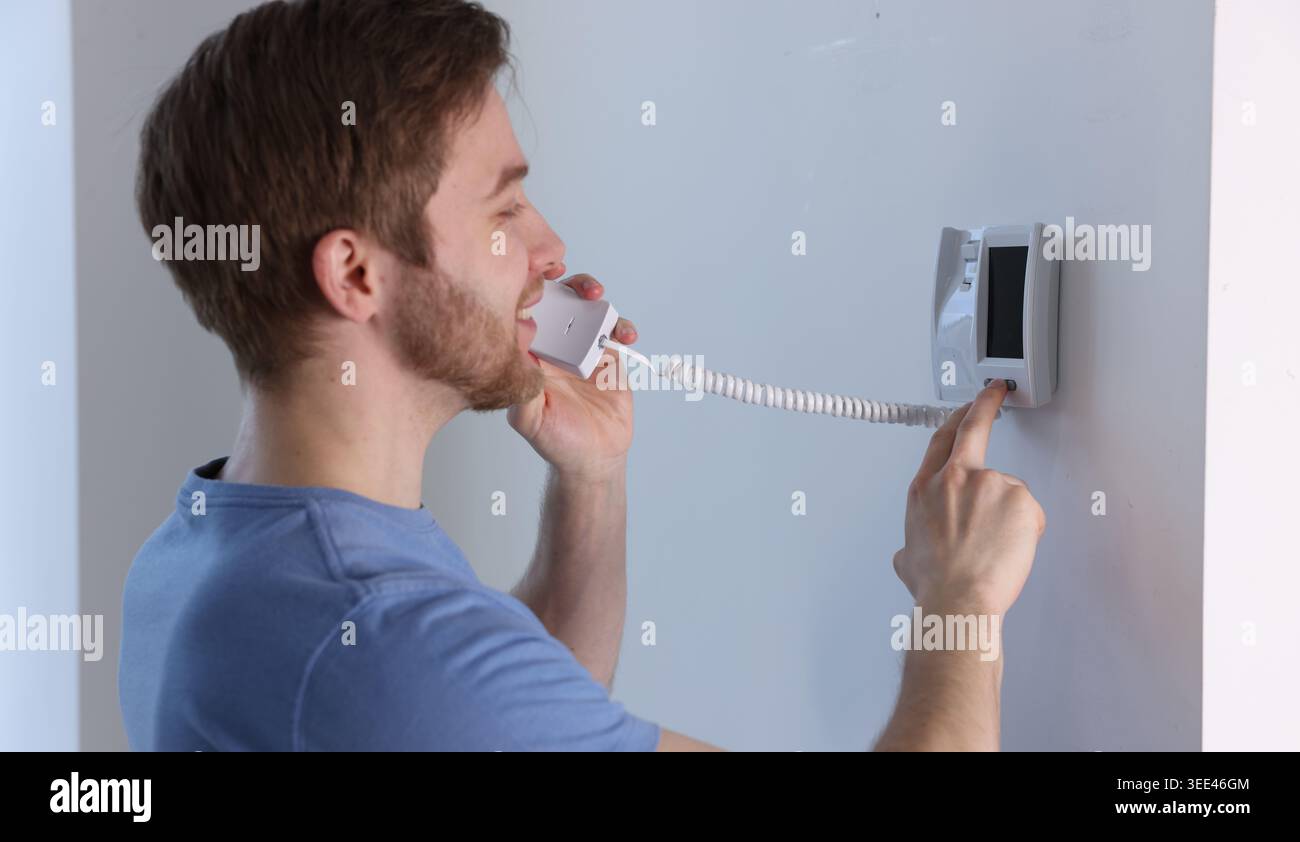 Man with handset pressing button on intercom panel indoors Stock Photo