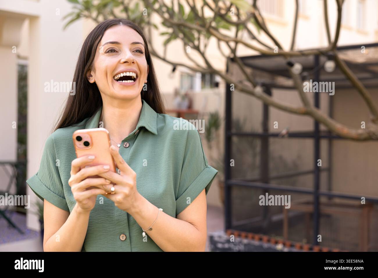 Smiling woman checking smartphone standing outside in house backyard Stock Photo