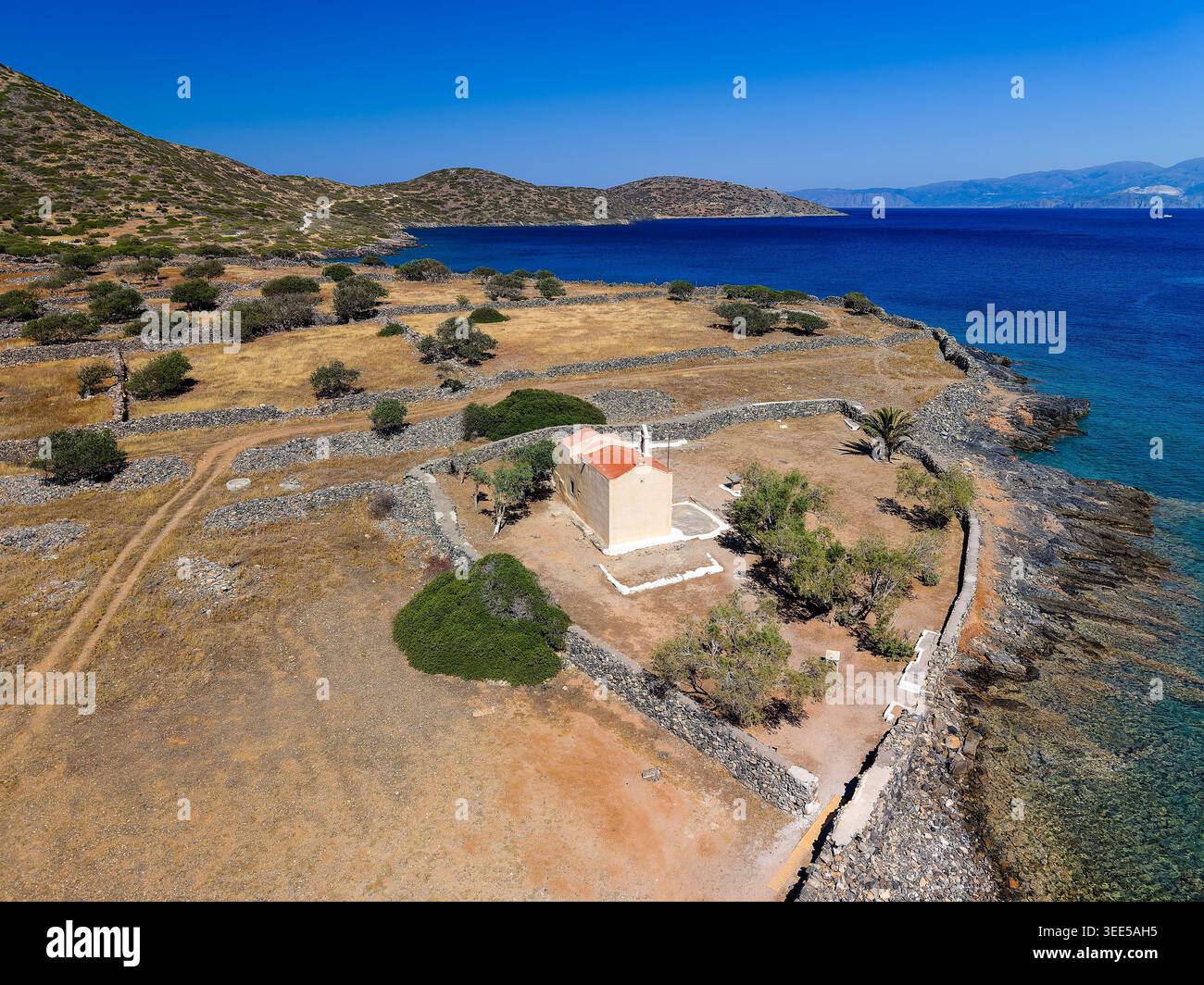 Scenic Mediterranean landscape featuring a lone church and rugged hills in summer Stock Photo