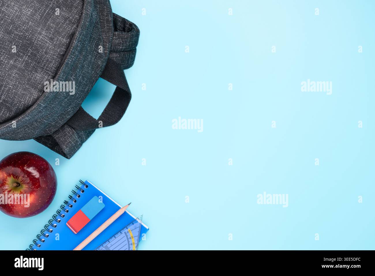 school supplies set backpack apple notebook and stationery on blue background copy space Stock Photo