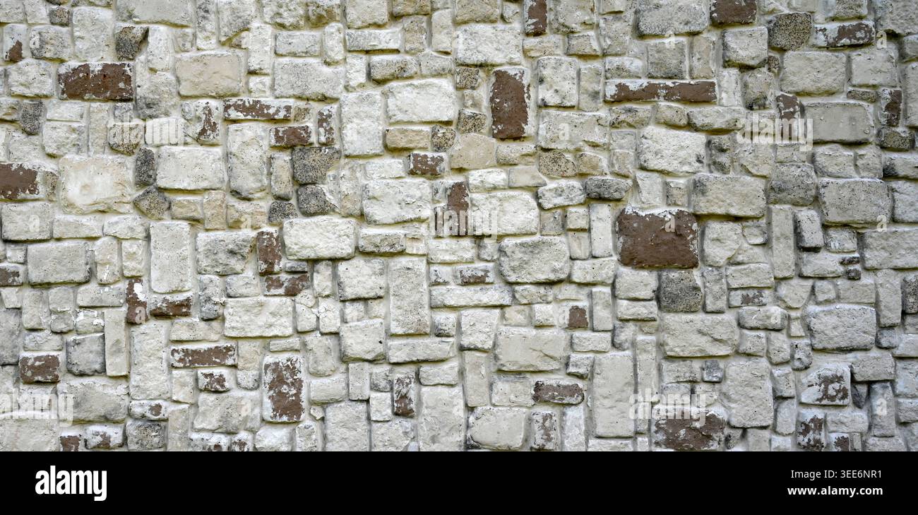 Stone wall surface with light gray, painted brown, and darker gray rectangular stones in various sizes Stock Photo