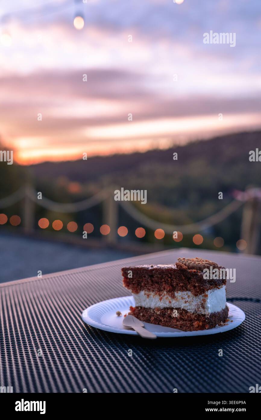 A delicious piece of chocolate layer cake with white cream served on a small plate outdoors Stock Photo