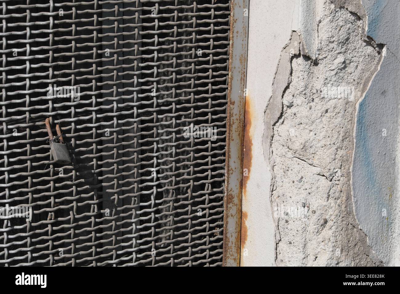 RUSTY METAL GRID TEXTURE BACKGROUND WITH A FRAGMENT OF RUINED AND PEELING URBAN WALL Stock Photo