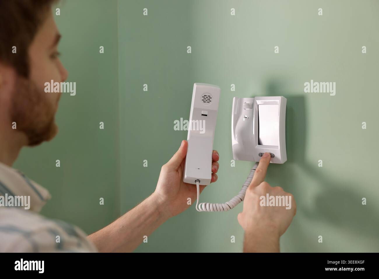 Man with handset pressing button on intercom panel indoors, closeup Stock Photo