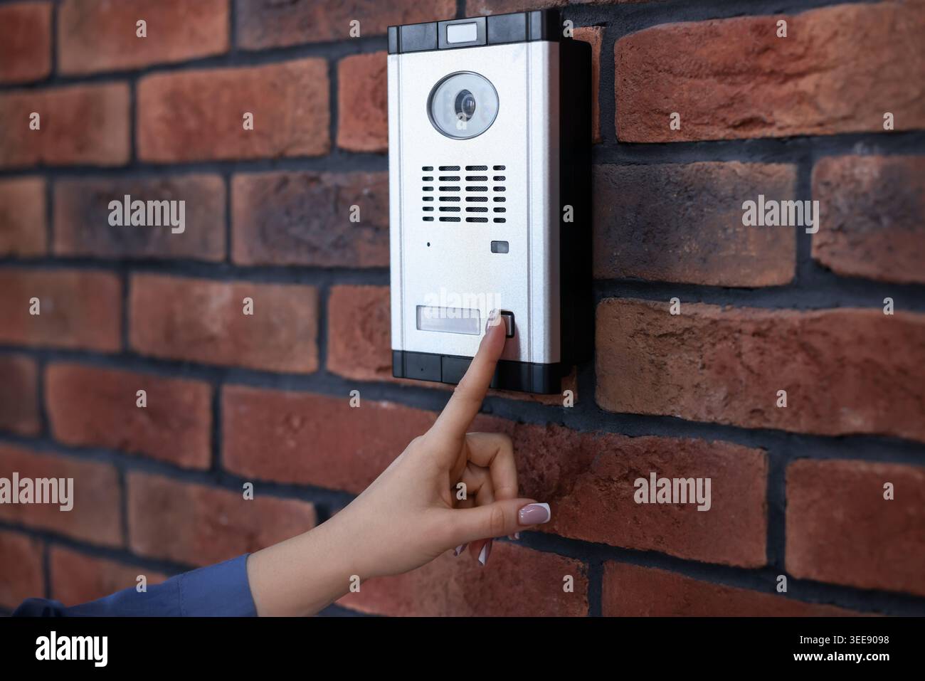 Woman pressing button on intercom panel near brick wall, closeup Stock Photo