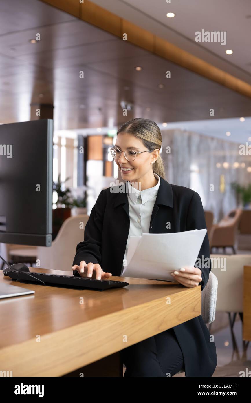 Female receptionist processing documents, using computer, working at front desk Stock Photo