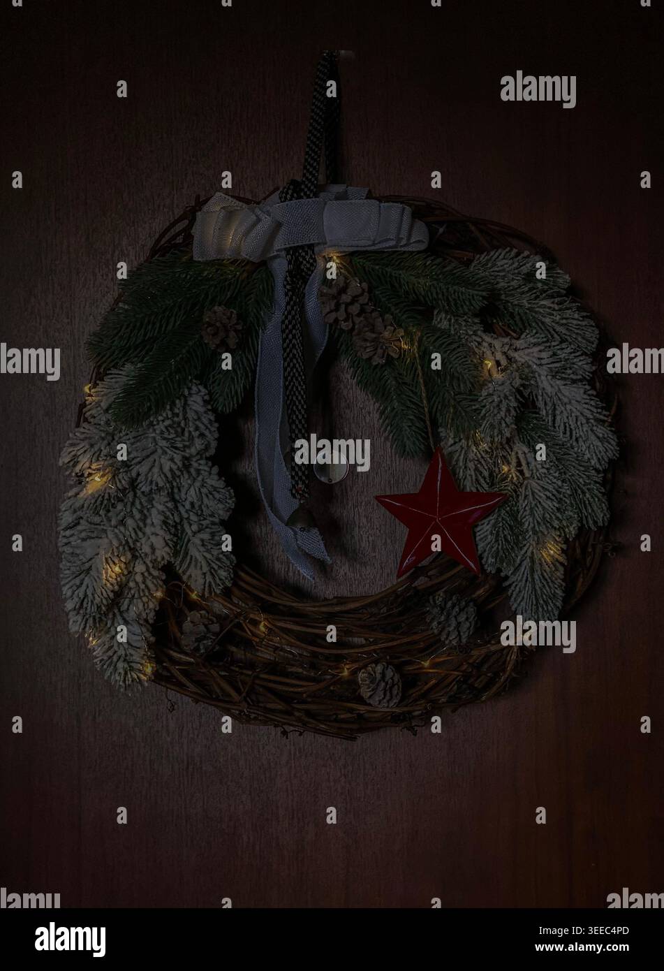 Christmas wreath with pine branches, pinecones and warm lights on wooden door - Smartphone Captured Stock Image