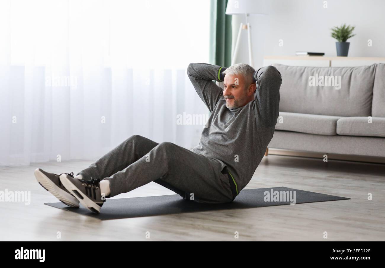 Athletic bearded senior man doing exercises for abs at home Stock Photo