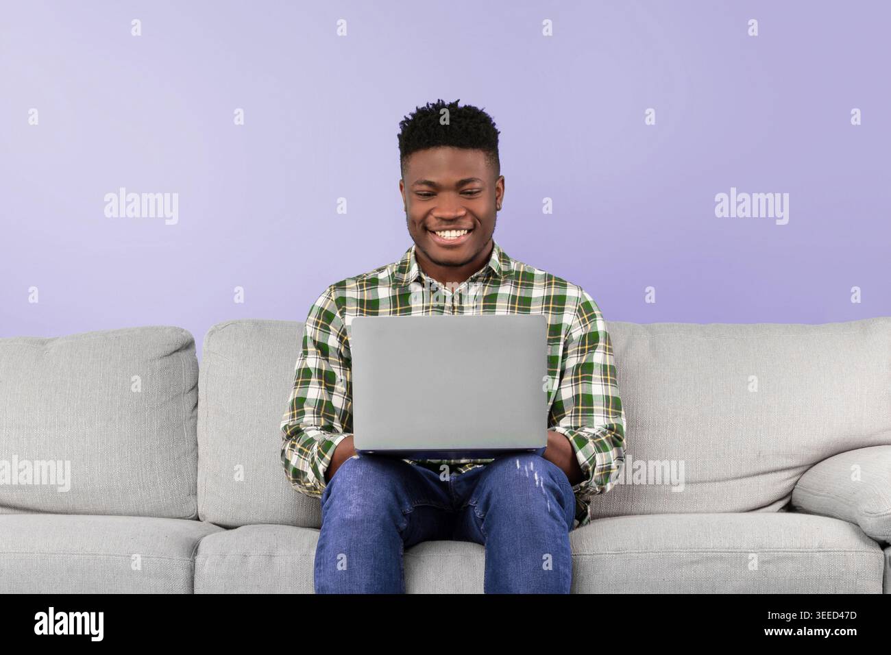 Smiling Man Using Laptop While Sitting on Gray Sofa in a Modern Indoor Setting Stock Photo
