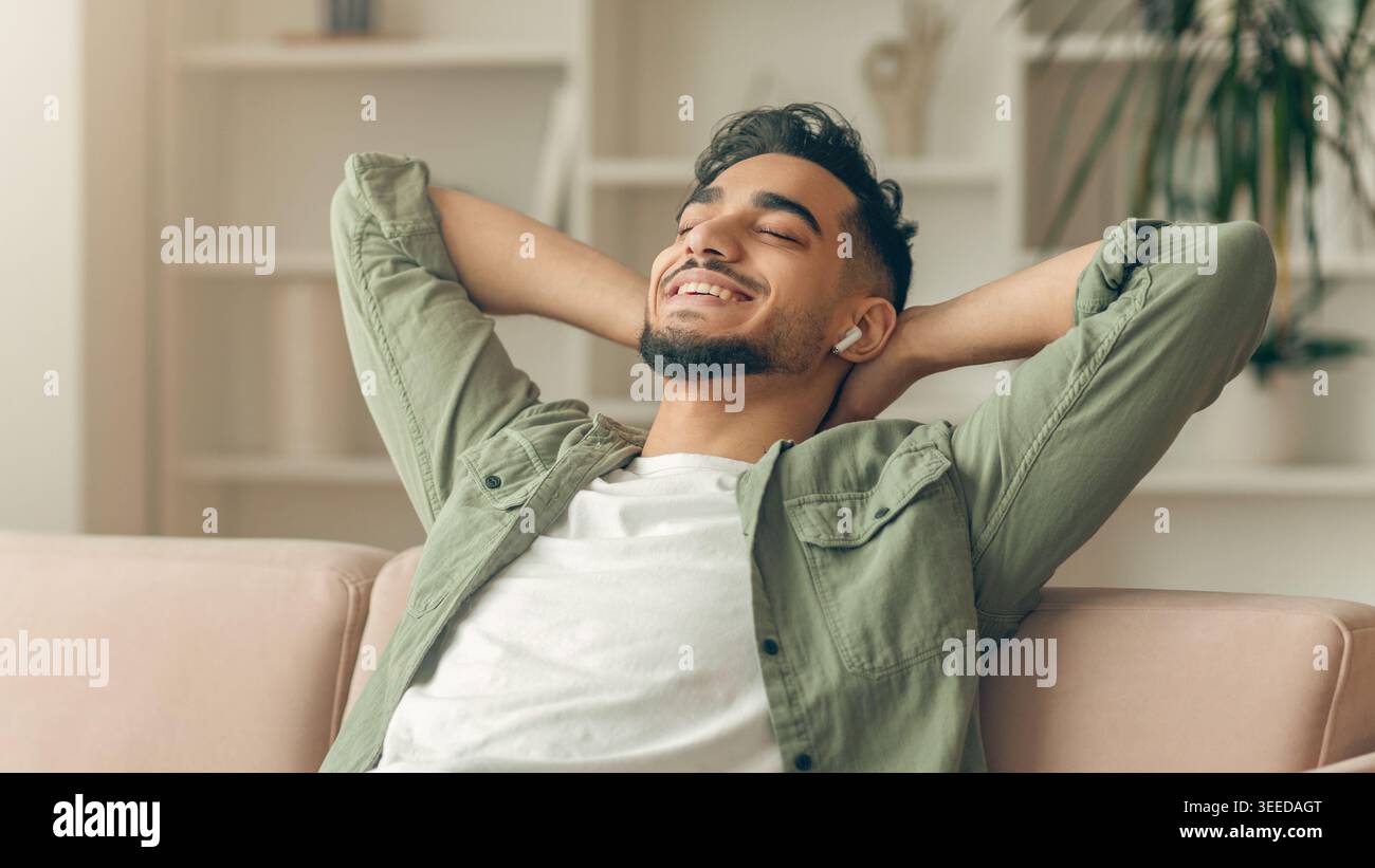 Man Relaxes on Sofa While Listening to Music in a Bright Room During the Day Stock Photo