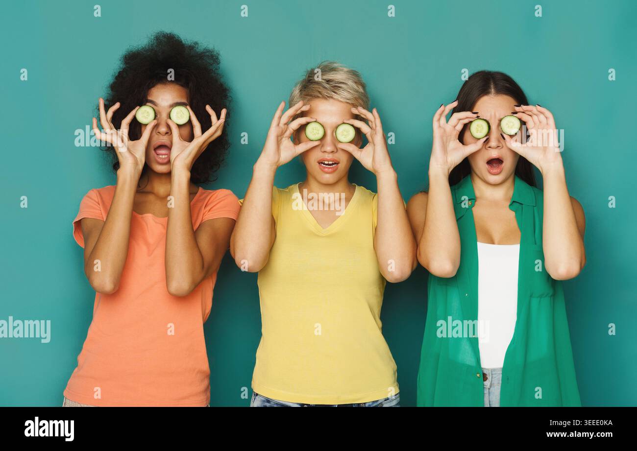 Three friends having fun with cucumbers in a colorful backdrop Stock Photo