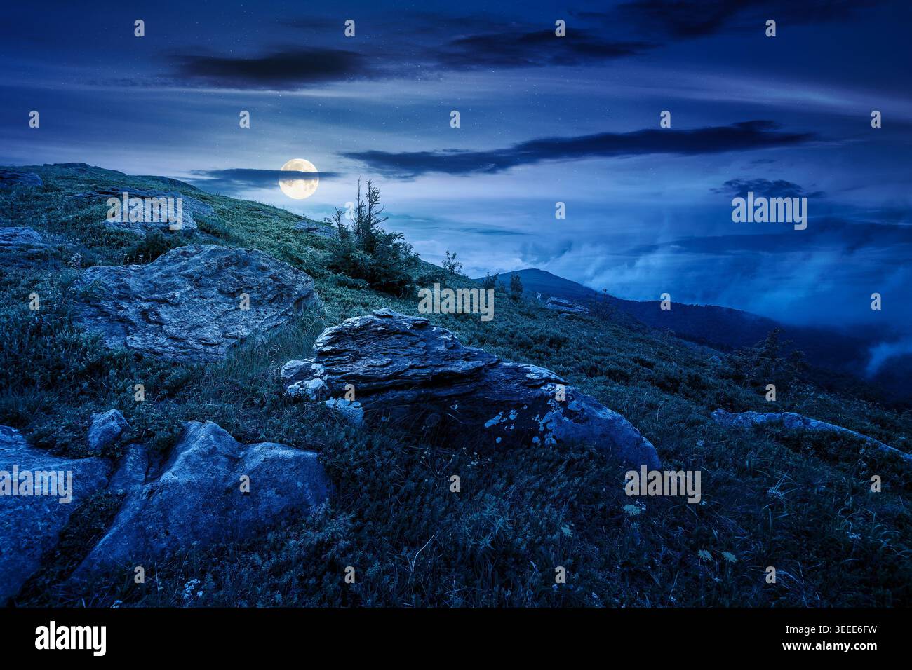 green landscape of mountain in summer at night. mysterious view of rock among grass on the hillside. full moon over travel background under a dark sky Stock Photo