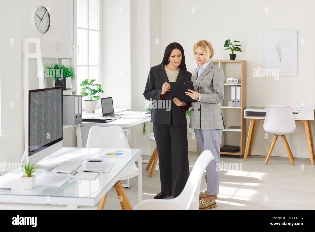 Two businesswomen discussing project in office while reviewing financial data on digital tablet. Stock Photo