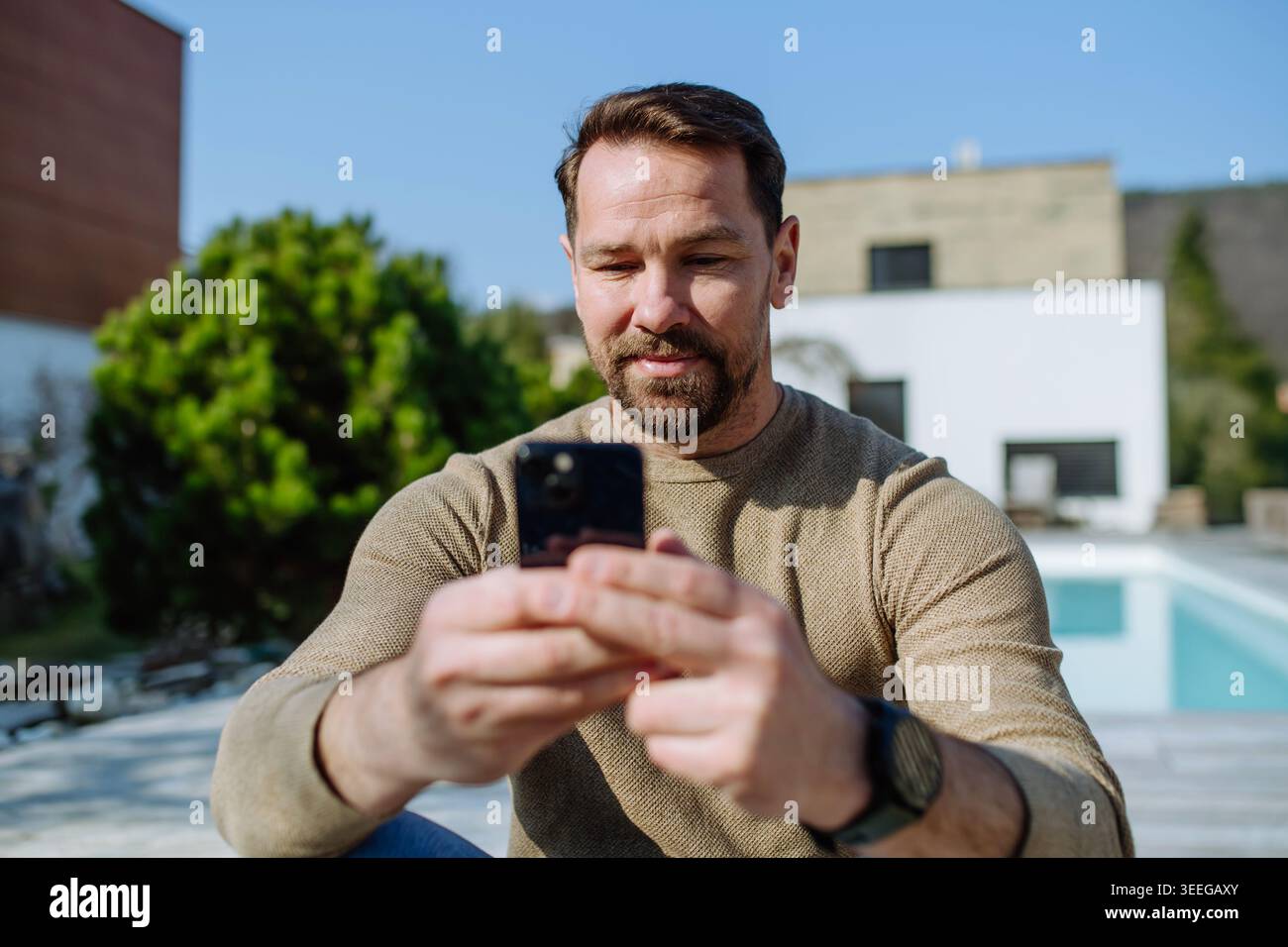 Man using smartphone in backyard and checking messages. Stock Photo