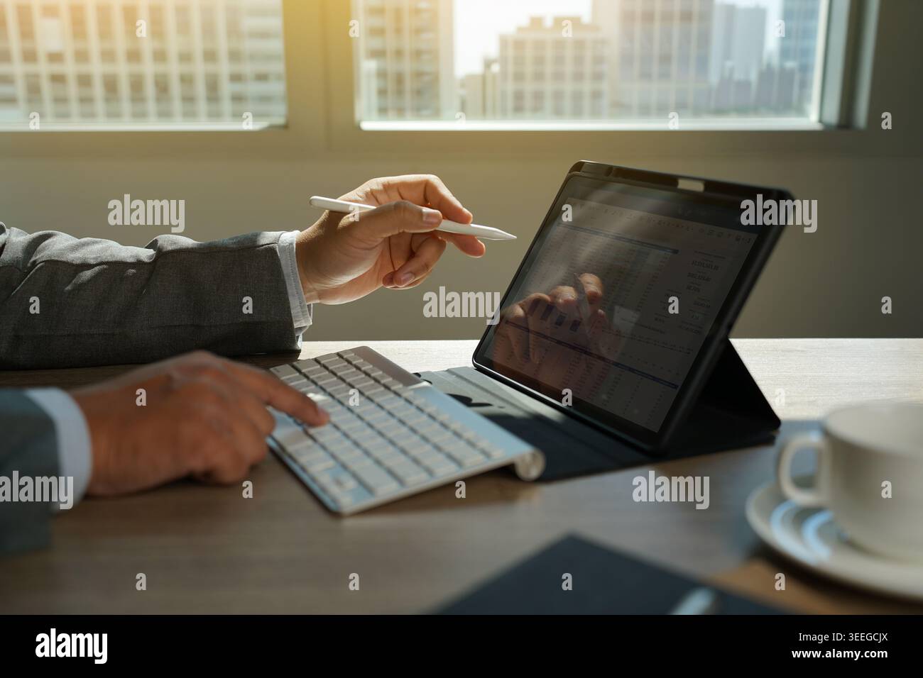 Hand using tablet with keyboard displaying financial chart data on desk, representing business analysis workflow, data reporting process, digital acco Stock Photo