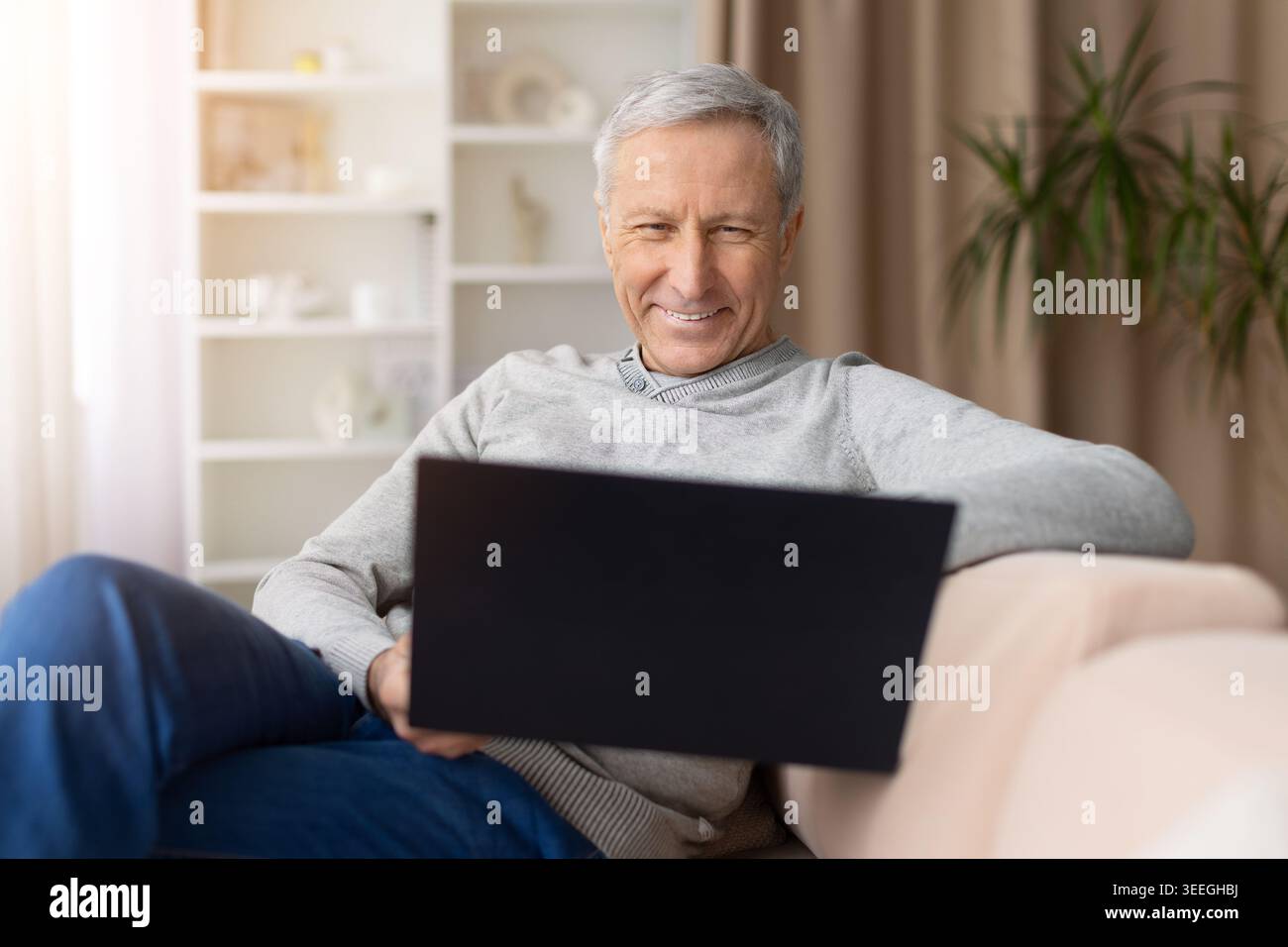 Smiling senior man relaxing at home while using laptop on sofa Stock Photo