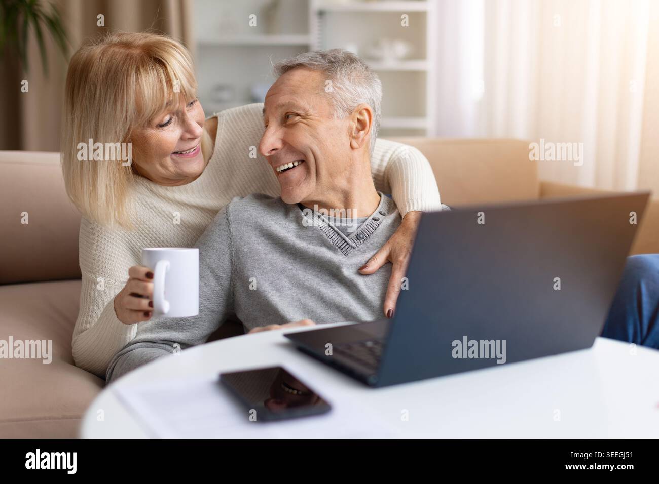 Happy senior couple using laptop while relaxing at home with coffee Stock Photo