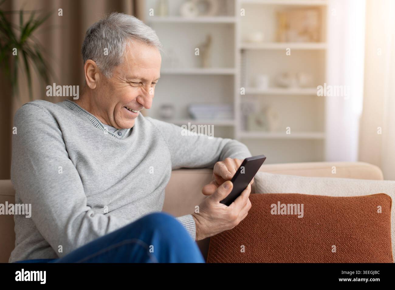Cheerful mature man using smartphone while sitting on sofa at home Stock Photo