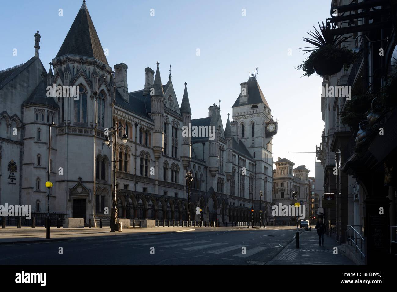 The Royal Courts of Justice in London, UK, at sunrise. A lone pedestrian walks past the historic landmark. Stock Photo