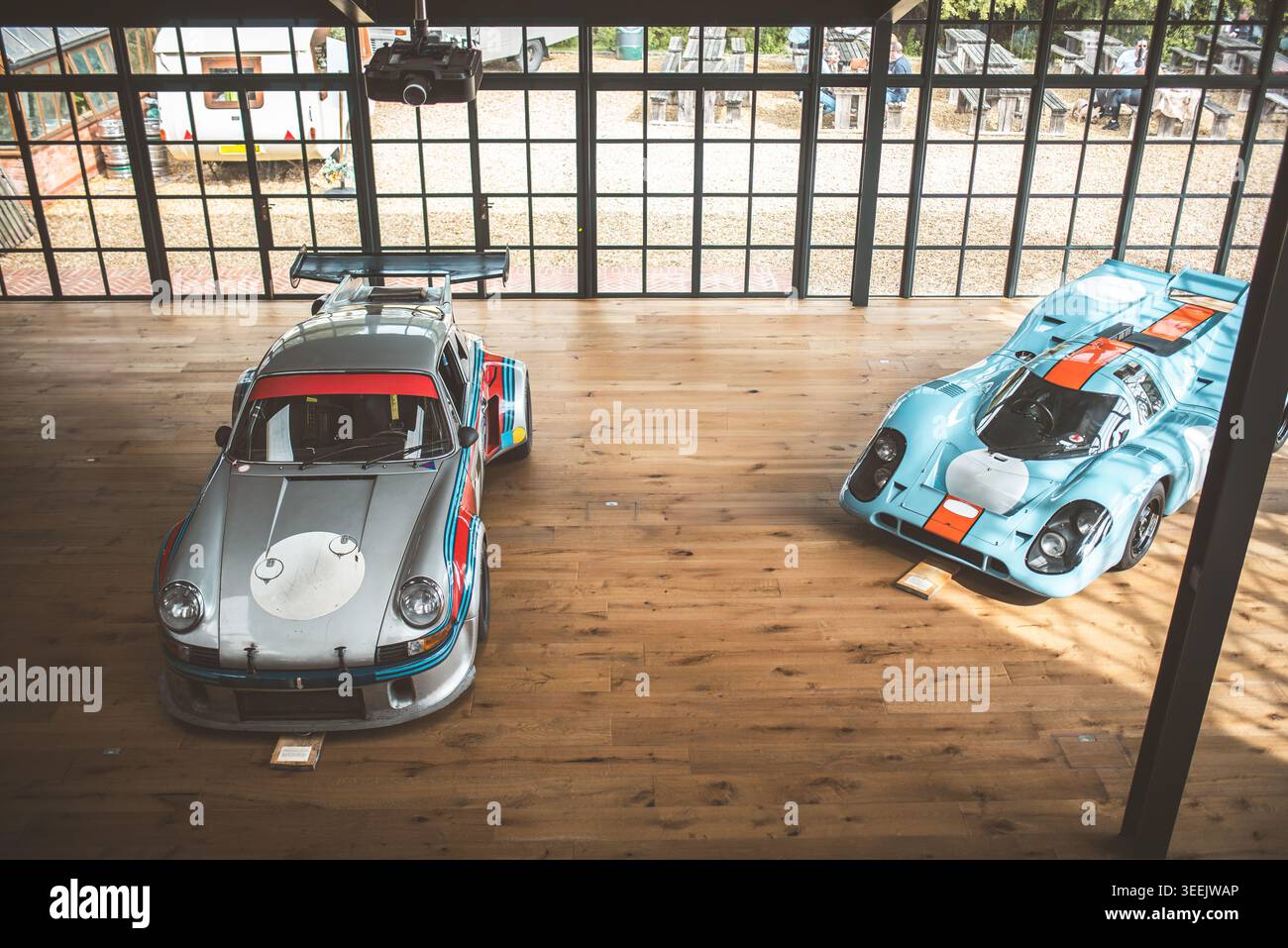 Two iconic race cars are showcased on a wooden floor, creating a ...