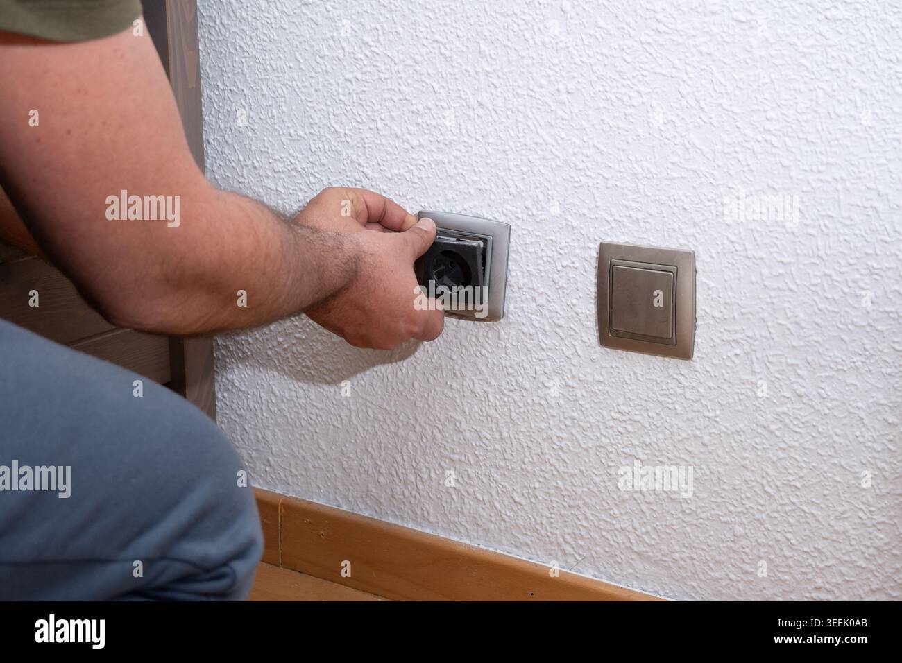 Person's hand installing or repairing an electrical socket on a white wall Stock Photo