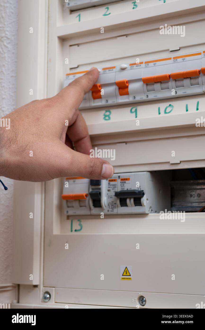 Hand activating power switch in electrical panel, checking electricity Stock Photo