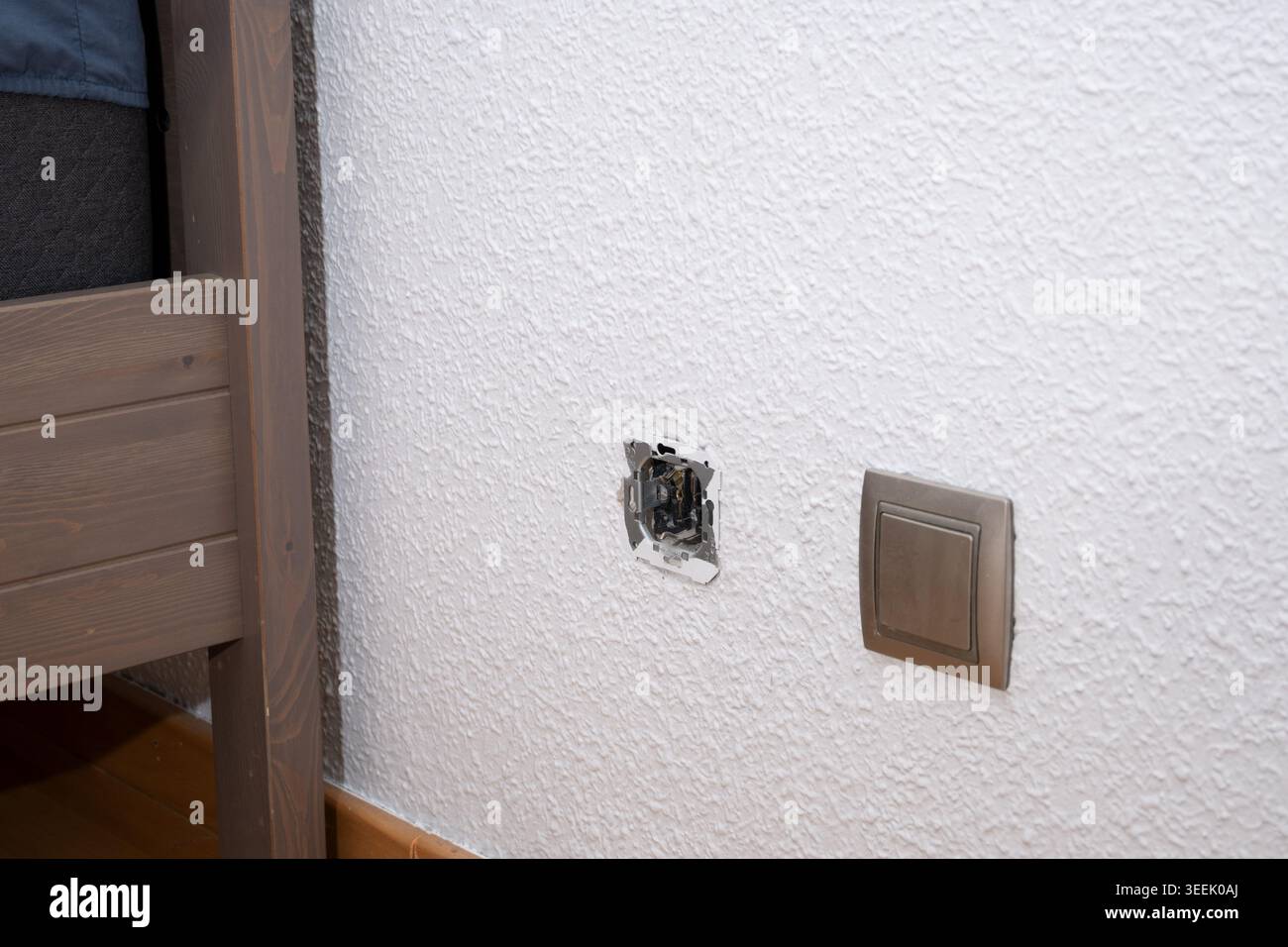 Exposed electrical wiring from a damaged wall socket on a textured white wall Stock Photo