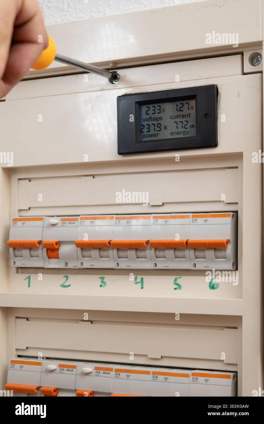 Hand installing smart meter displaying voltage, current, power, and energy in electrical panel Stock Photo