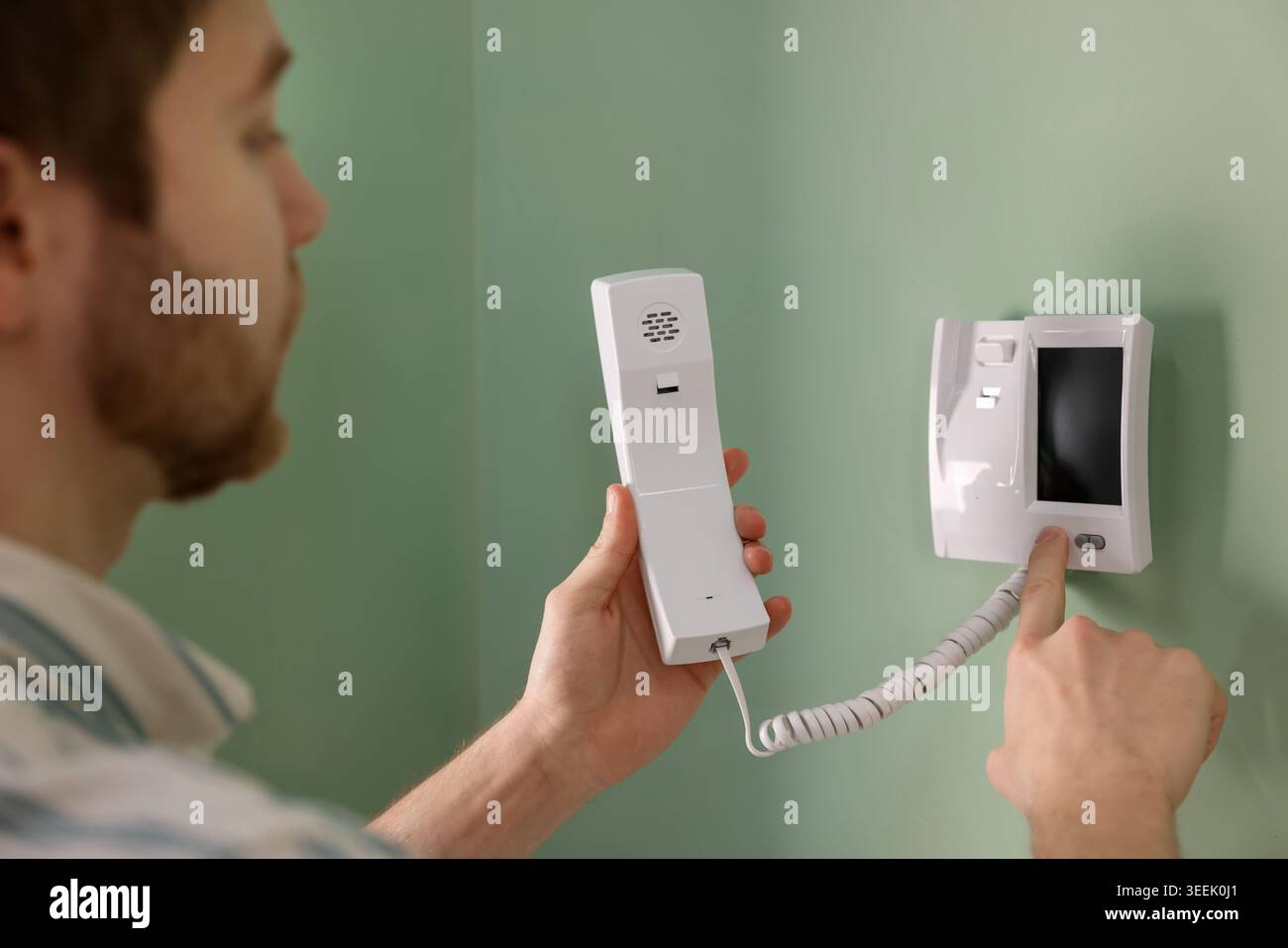 Man with handset pressing button on intercom panel indoors, closeup Stock Photo