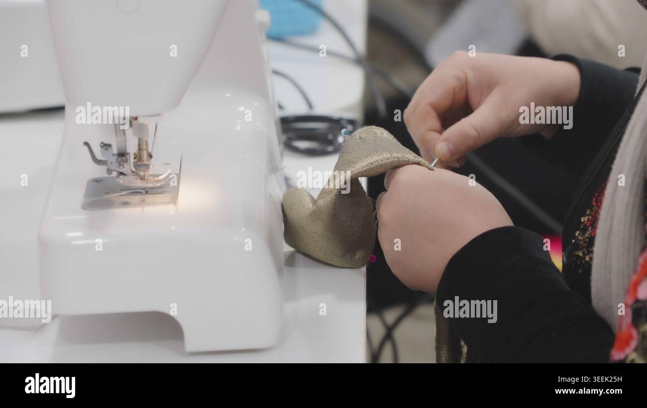 Woman using sewing machine while guiding fabric through needle in workshop in pr Stock Photo