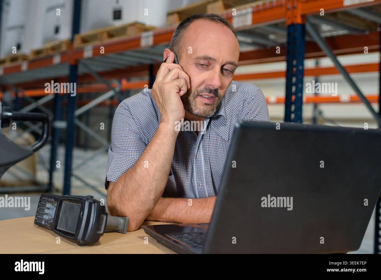 warehouse worker with laptop and scanner using smartphone Stock Photo