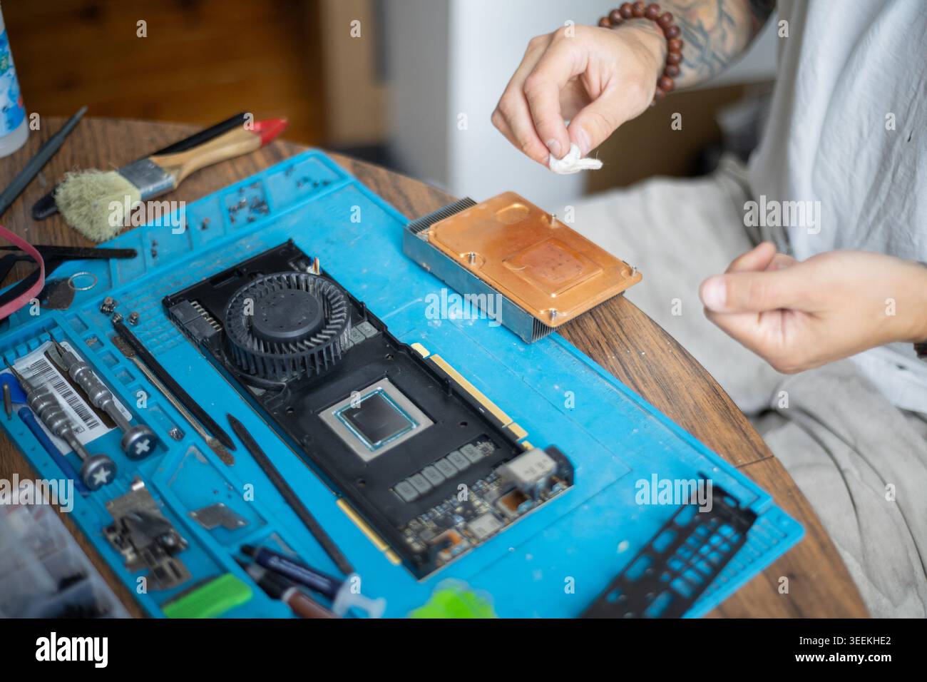 Person repairs a computer graphics card on a blue workbench in a well-lit indoor space during the day Stock Photo