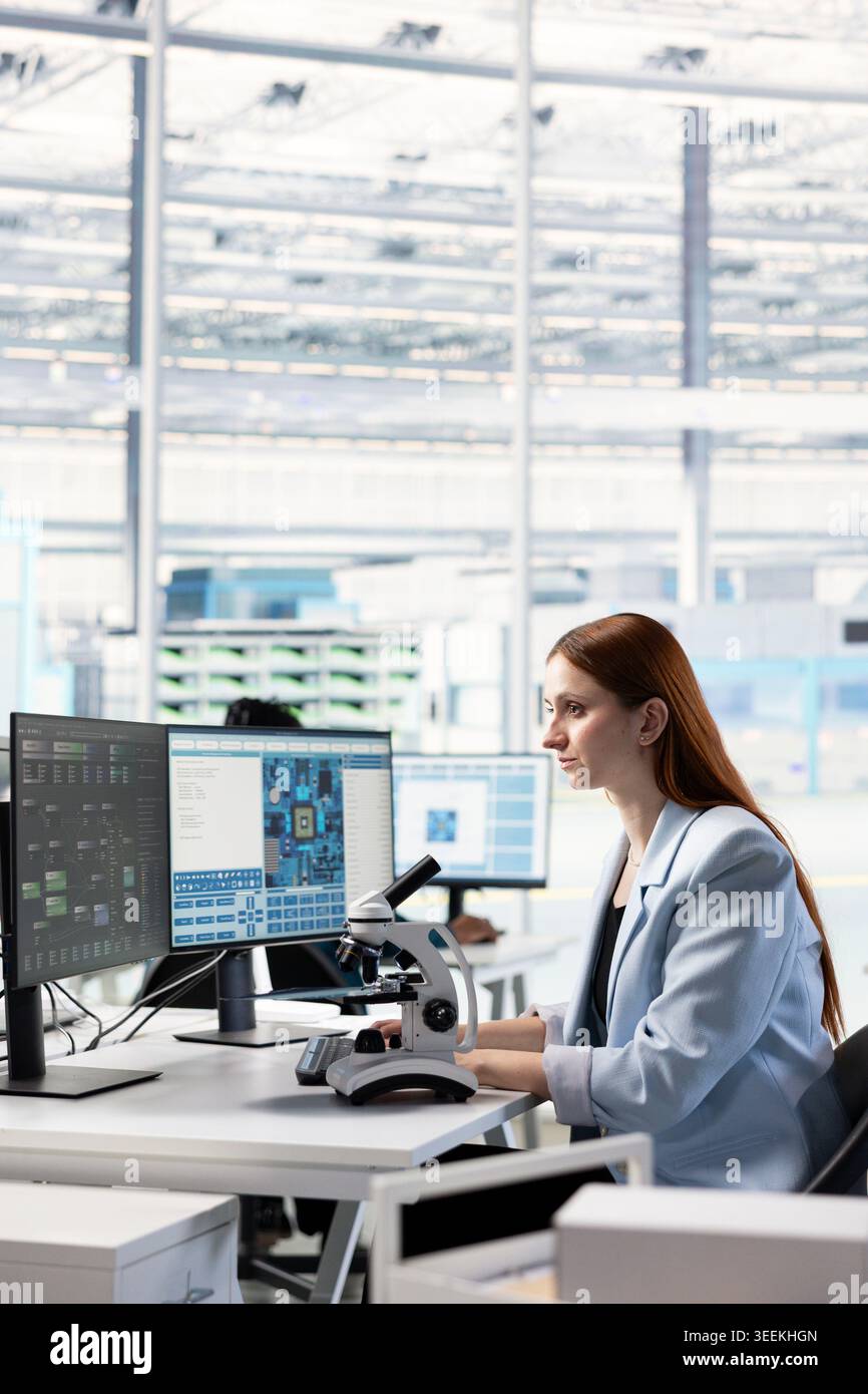 Female technician observing microchip layout with microscope in RD office. Engineer doing innovative study using microscopy tool, researching materials for nanotechnology development Stock Photo