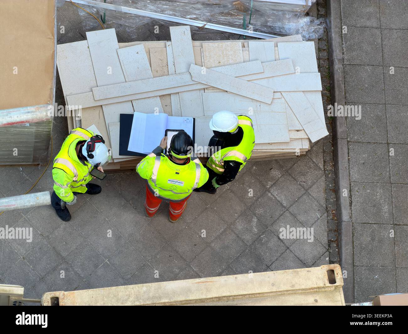Three workers in high visibility jackets discuss documents at construction site together Stock Photo